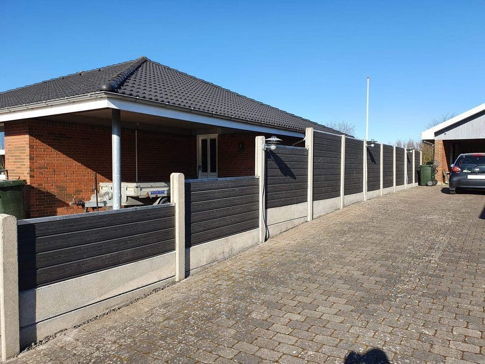 Niedriger WPC-Zaun in dunkler Holzstruktur zwischen Betonpfosten an einer gepflasterten Einfahrt