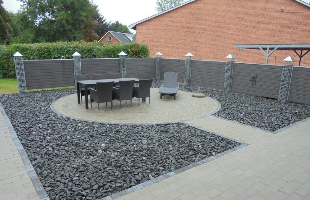 Moderne Kiesterrasse, eingefasst von grauem WPC-Sichtschutz mit Gabionen-Pfeilern