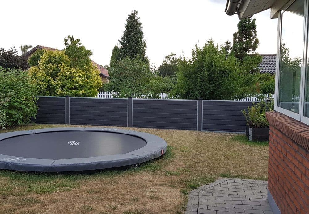 Niedriger WPC-Zaun in Anthrazit als Gartenbegrenzung hinter einem Bodentrampolin