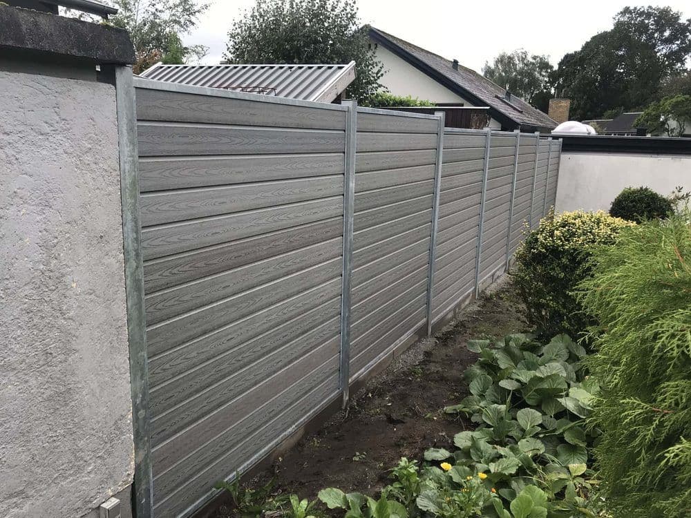 Hoher WPC-Sichtschutzzaun in Betongrau mit Holzstruktur auf feuerverzinkten Stahlpfosten vor einer verputzten Mauer